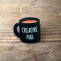 Nyssa Creative Fuel pin featuring vibrant colors and intricate design, perfect for accessorizing bags or clothing.
