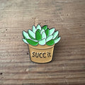 Nyssa "Suck it" pin featuring bold text design, made of metal with colorful enamel finish, perfect for accessories or collection.