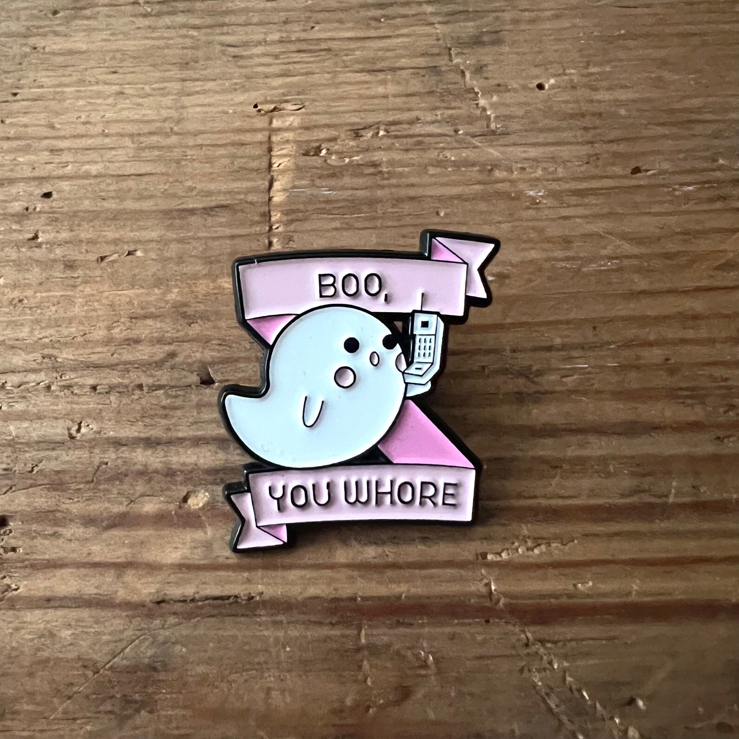 Nyssa "Boo, you whore" enamel pin featuring bold text on a metallic backing, perfect for accessorizing bags or jackets.