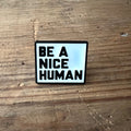 Nyssa "Be a nice human" pin showing a colorful enamel pin with positive message and playful design.