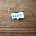 Bright yellow "Yeah!" pin by Nyssa featuring bold text and a playful design, perfect for accessorizing clothing or bags.