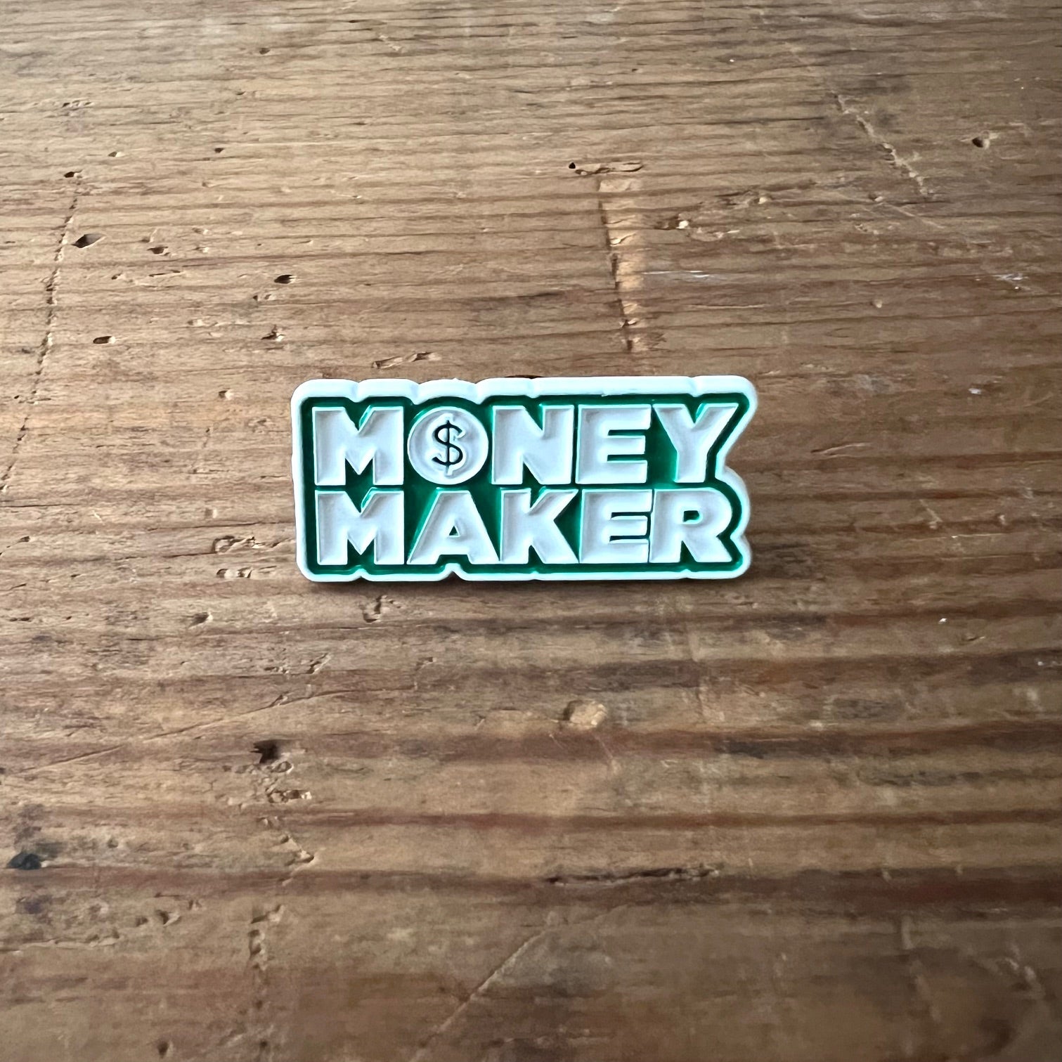 Nyssa Money Maker pin featuring a gold-colored design with bold lettering, perfect for accessorizing and making a statement.