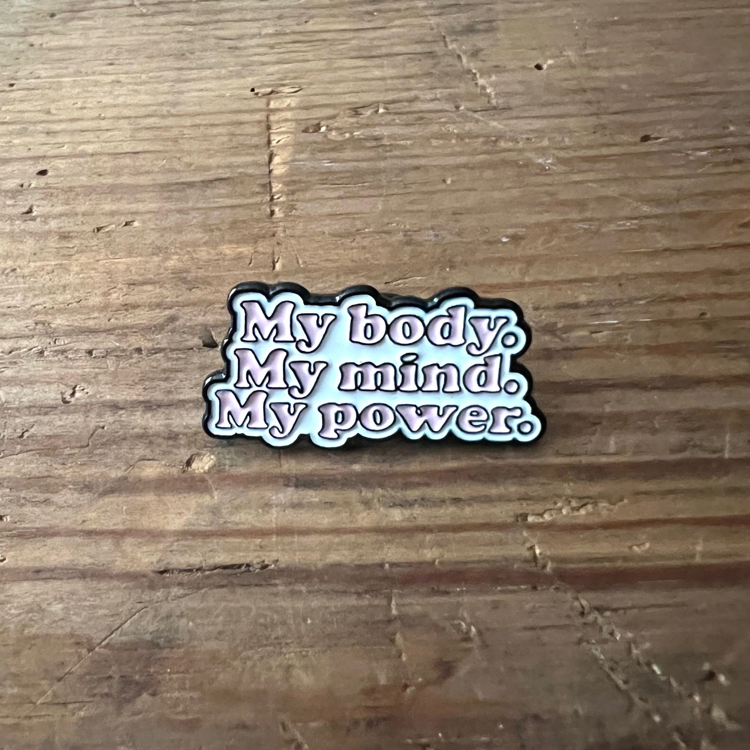 Nyssa "My body. My mind. My power" pin featuring bold text on a metal pin with a butterfly clasp.
