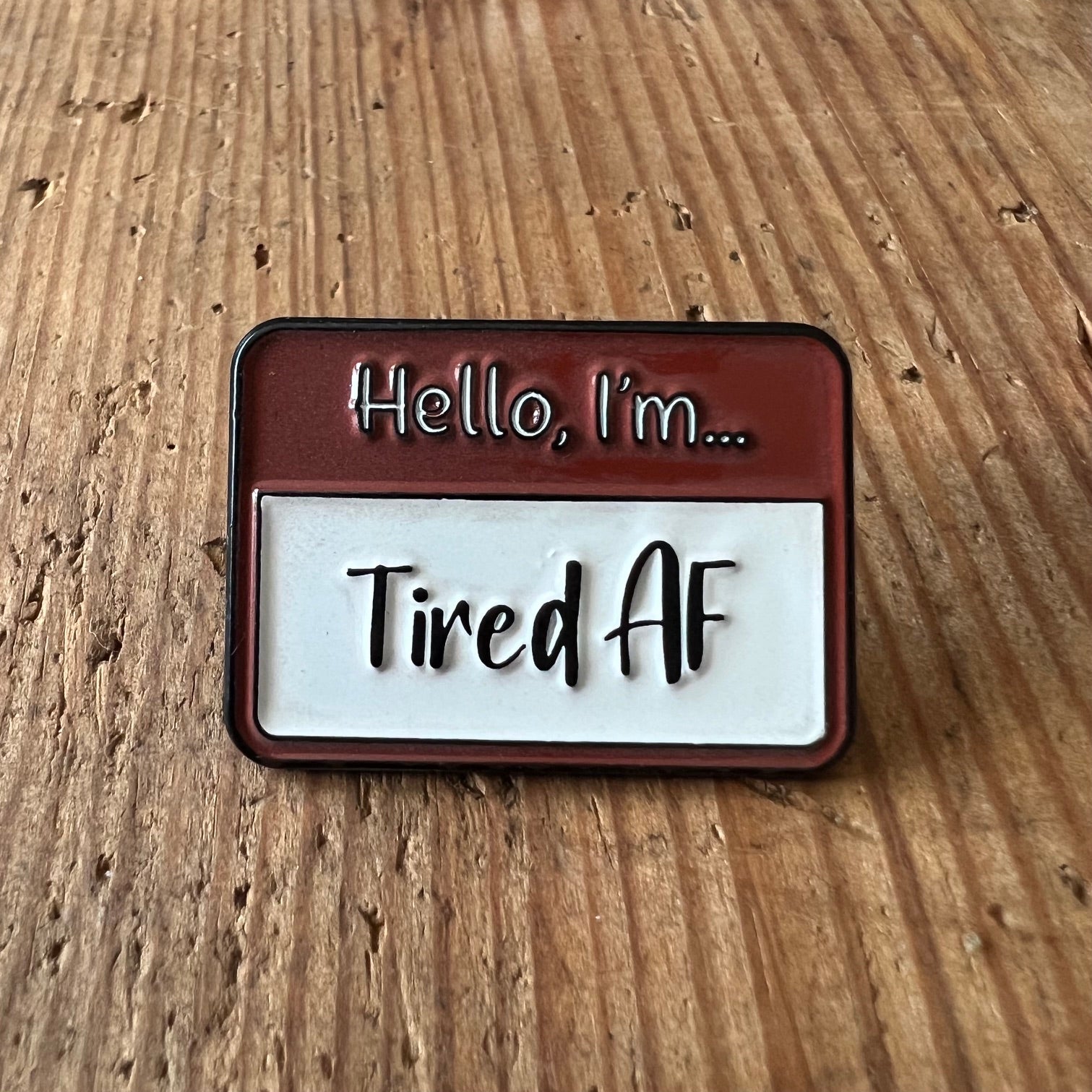 Nyssa Tired AF pin showing a small metal pin with bold "Tired AF" text on a white background.