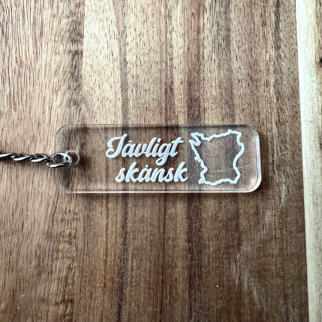 Nyssa Skåne keyring featuring the Jävligt skånsk logo with a metal ring and engraved design on a white background.