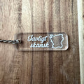 Nyssa Skåne keyring featuring the Jävligt skånsk logo with a metal ring and engraved design on a white background.