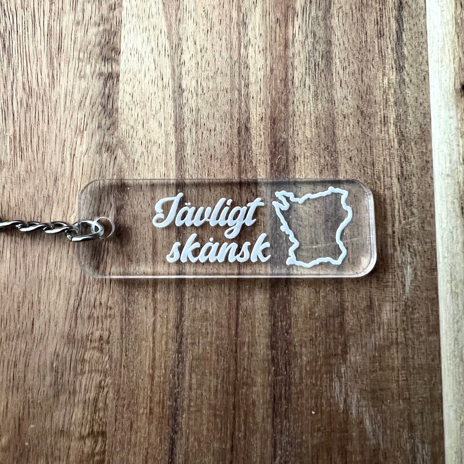 Nyssa Skåne keyring featuring the Jävligt skånsk logo with a metal ring and engraved design on a white background.