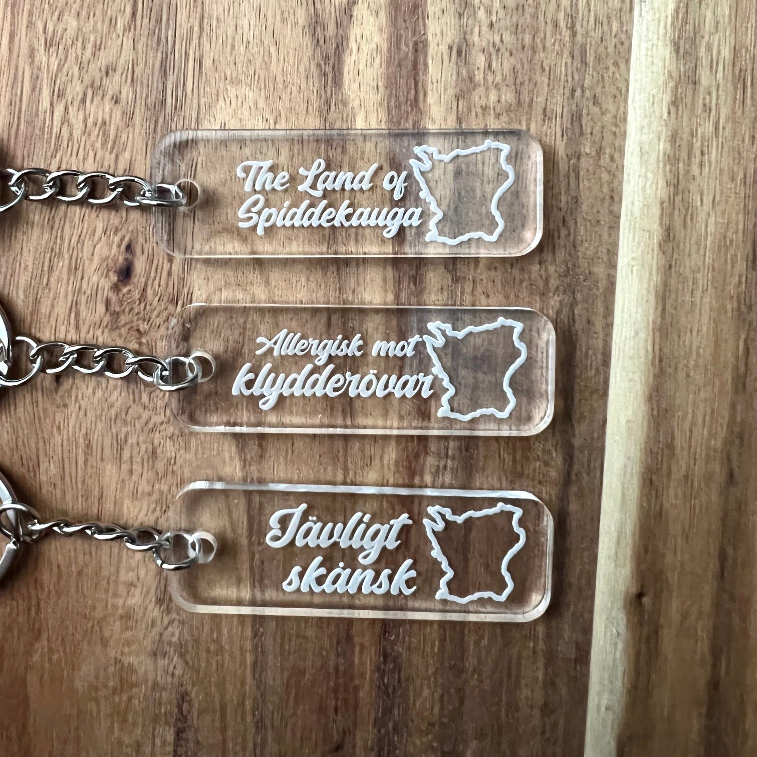 Nyssa Skåne keychain featuring a Jävligt skånsk design with a metal keyring and engraved details on a white background.