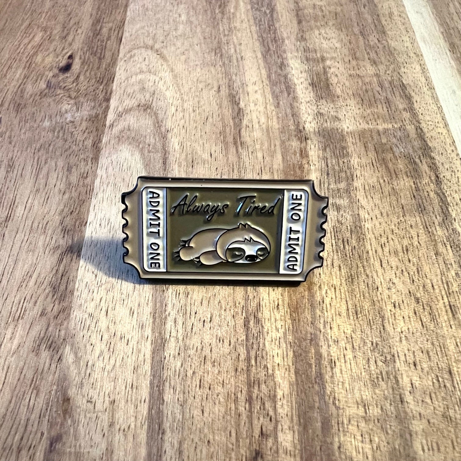 Nyssa Always Tired pin showing a humorous design with bold text on a metal pin for accessories and clothing.