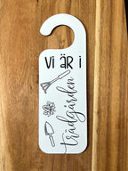 Nyssa Dörrhänge skylt with "Vi är i trädgården" text, featuring garden-themed design, hanging indoors or outside.