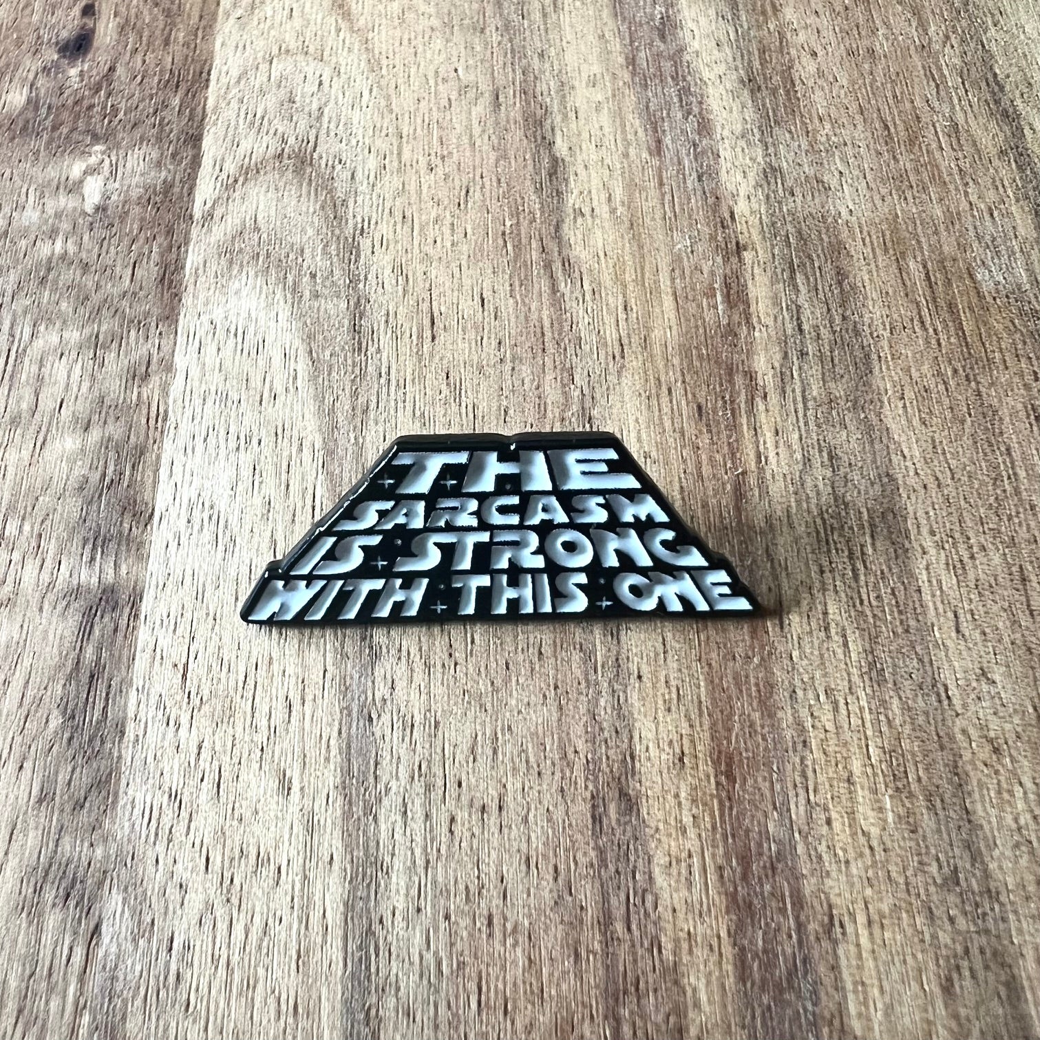 Nyssa Sarcasm Pin showing a humorous metal lapel pin with sarcastic design and branding on a white background.