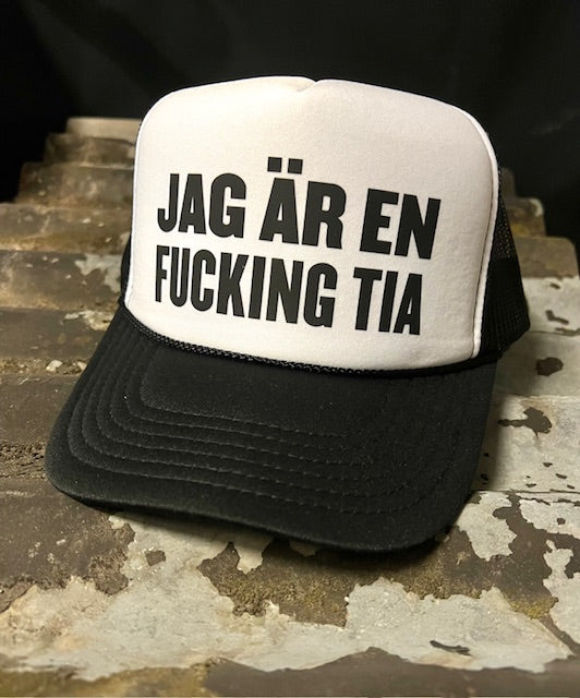 Nyssa trucker keps with bold "JAG ÄR EN FUCKING TIA" slogan, featuring mesh back and adjustable snap closure.